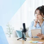 女性配信者が配信機材を前に企画内容をノートへまとめている