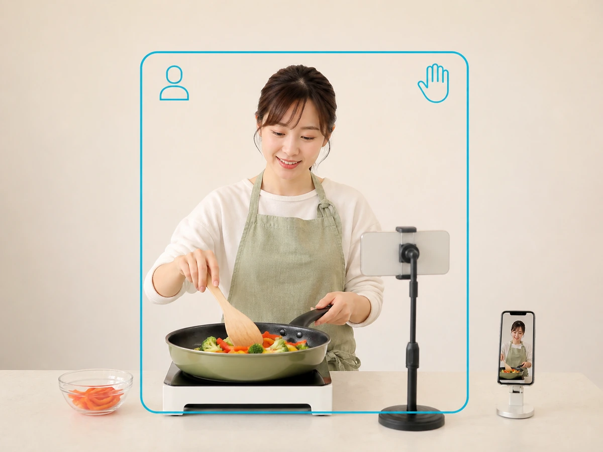 女性配信者がキッチンで顔とフライパンを動かす手元の両方が映る位置を別のスマートフォンで確認している