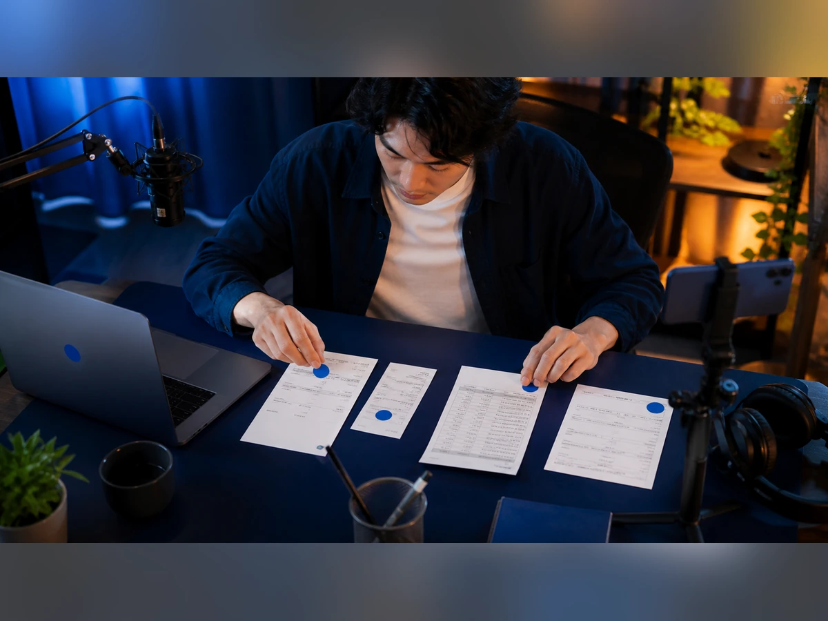 成人男性ライバーが支払明細、領収書、帳簿、銀行明細に同じ目印を付ける場面